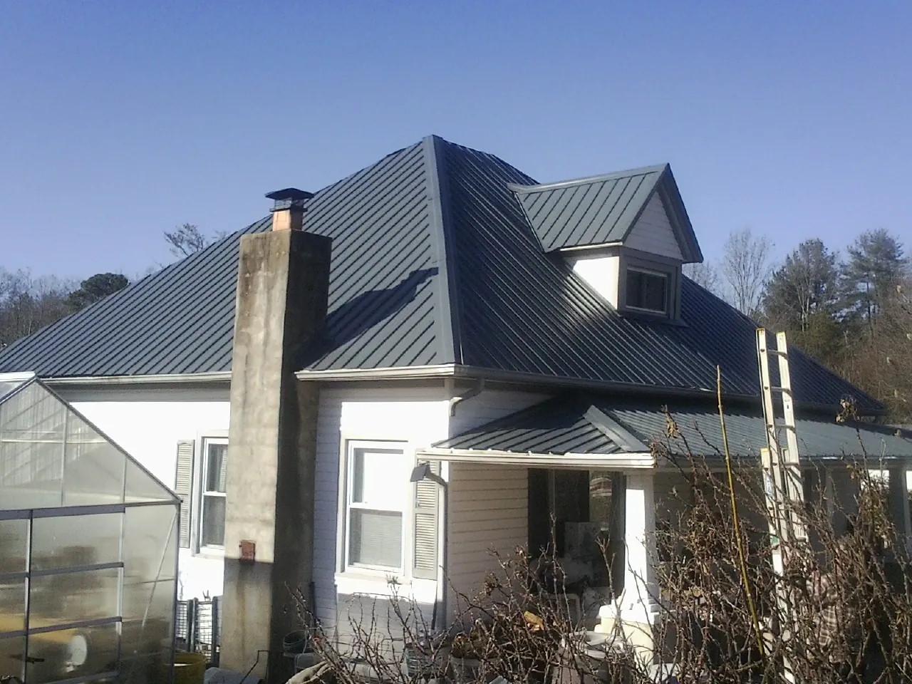 Dark blue standing seam metal roof on a white farmhouse with dormer — Slate & Tile Roof Repair by Roofing Brothers in Coulter