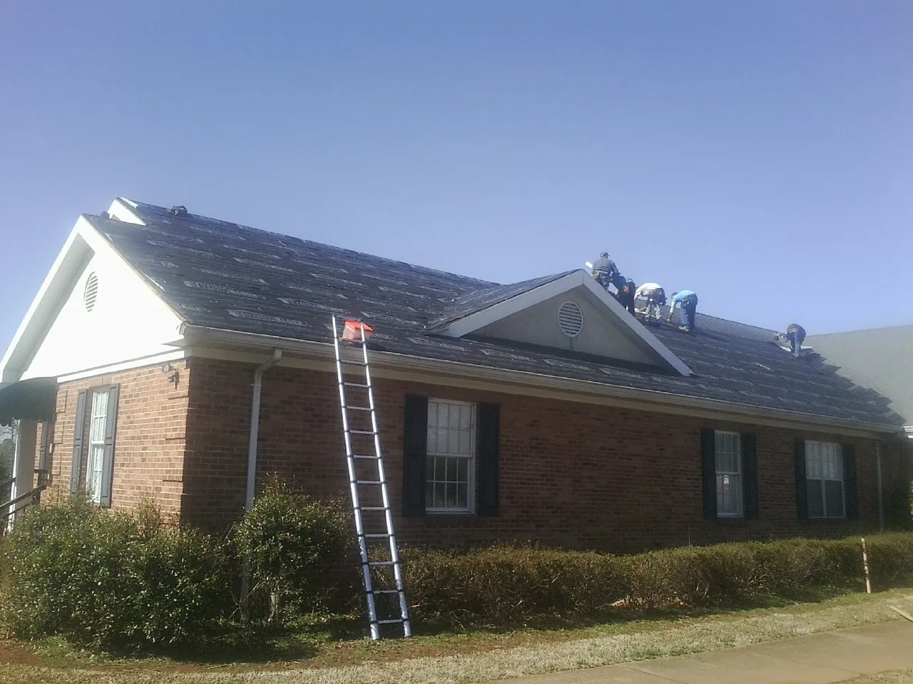 Crew tearing shingles off a brick ranch roof with a ladder set — Emergency Roof Repair work by our crew in Coulter