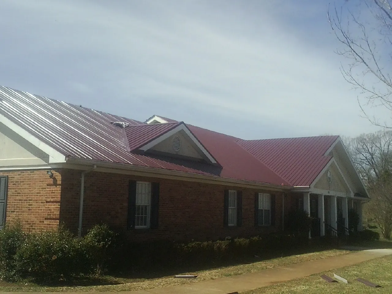 Red metal roof with gabled entries on a long brick building, from a Hail Damage Roof Repair job in Coulter