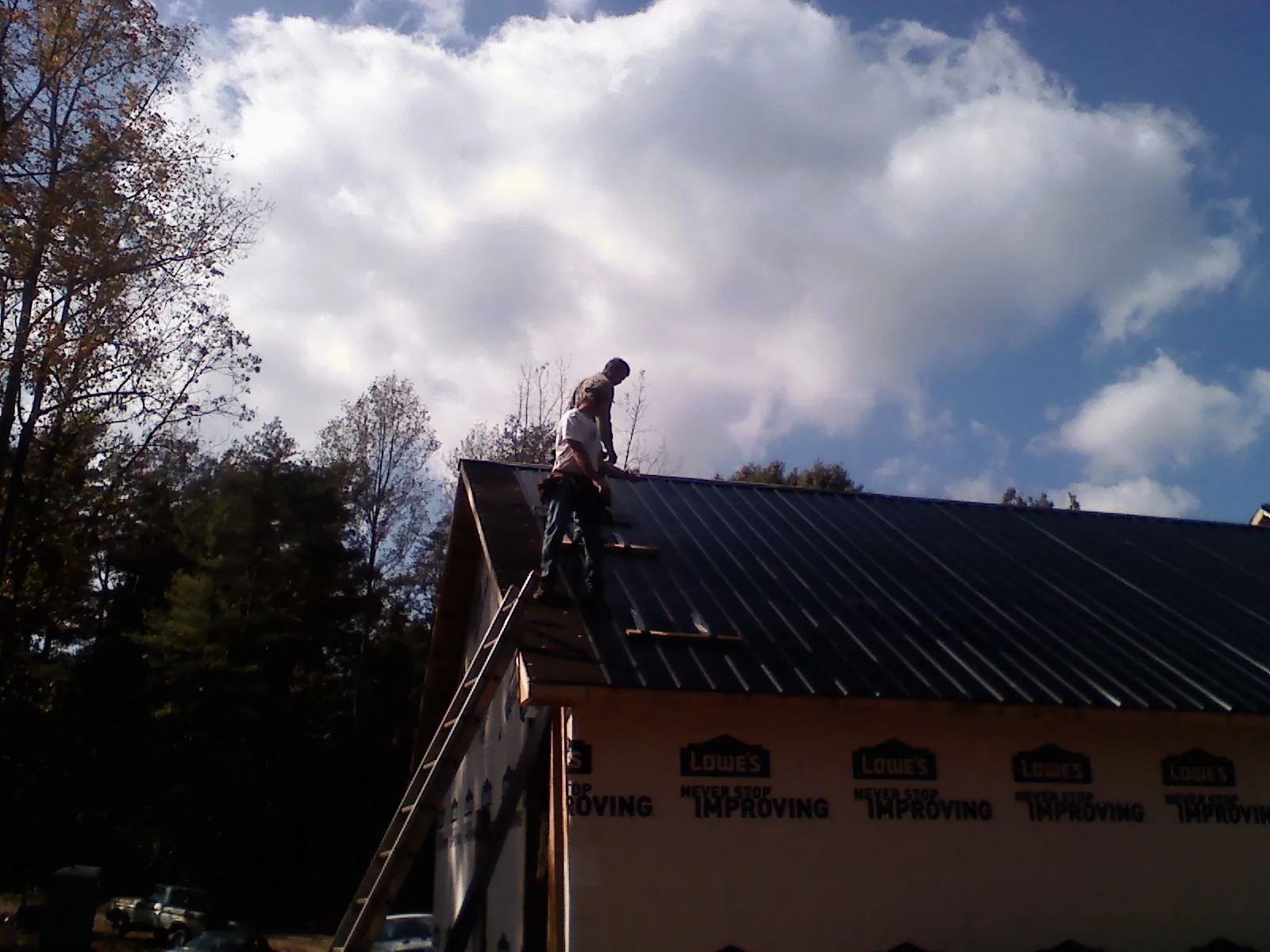 Roofer fastening dark metal panels high against a cloudy sky, from a Roof Inspection job in Coulter