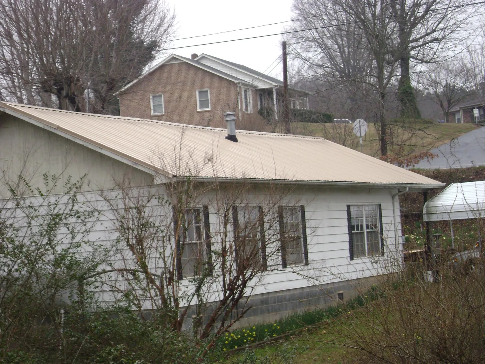 Tan metal roof on a white sided house set into a hillside — Commercial Roofing by Roofing Brothers in Coulter