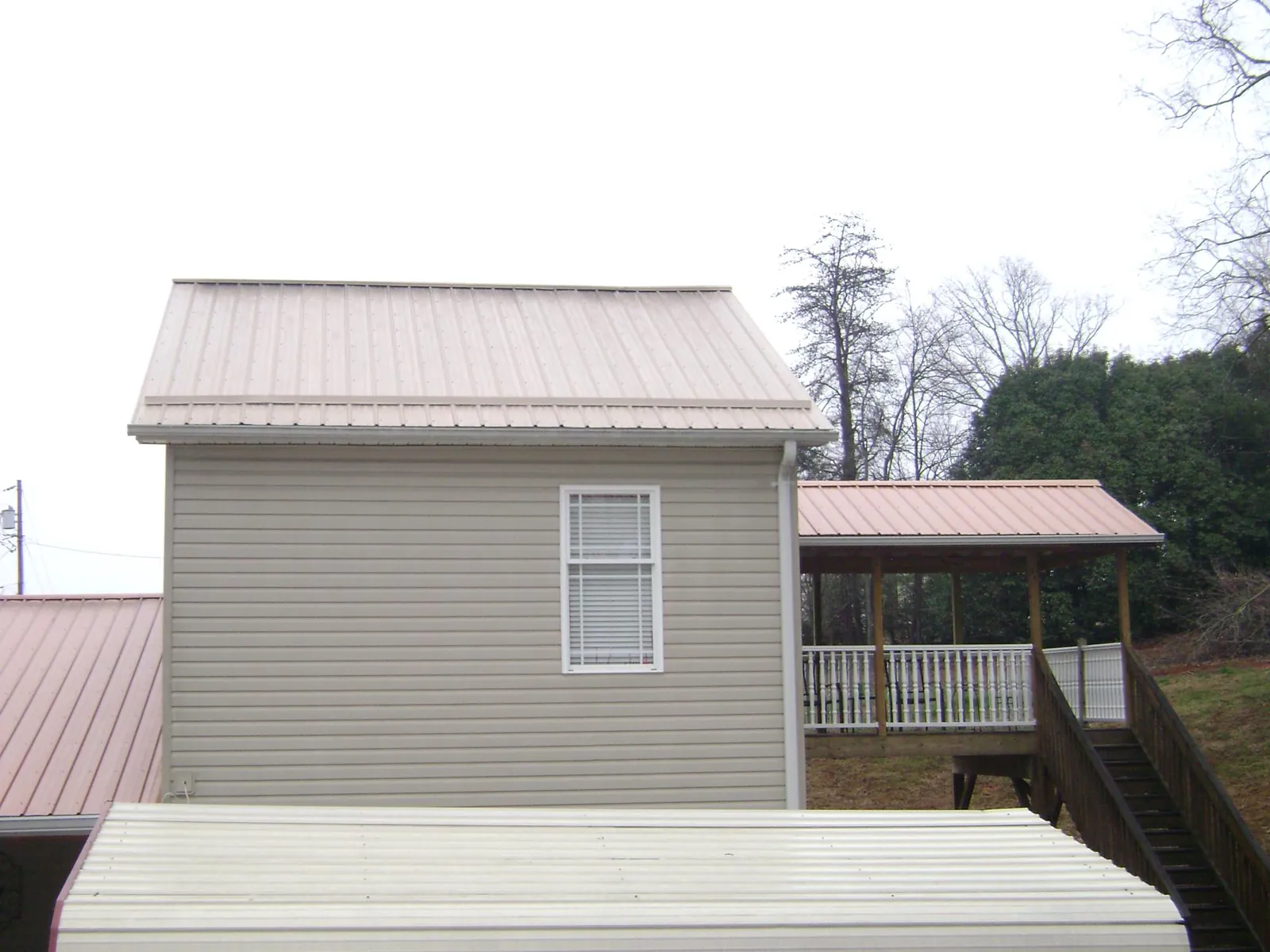 Tan metal roofs on a two story addition and attached porch, from a Roof Replacement job in Coulter